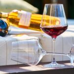 Copa de vino tinto sobre una barrica con viñedos españoles al fondo